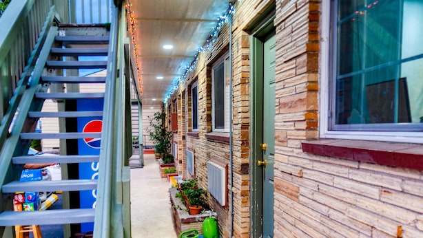 A narrow corridor with a staircase on the left, a brick wall on the right, and string lights overhead. - Budget Inn Motel (The Dalles)