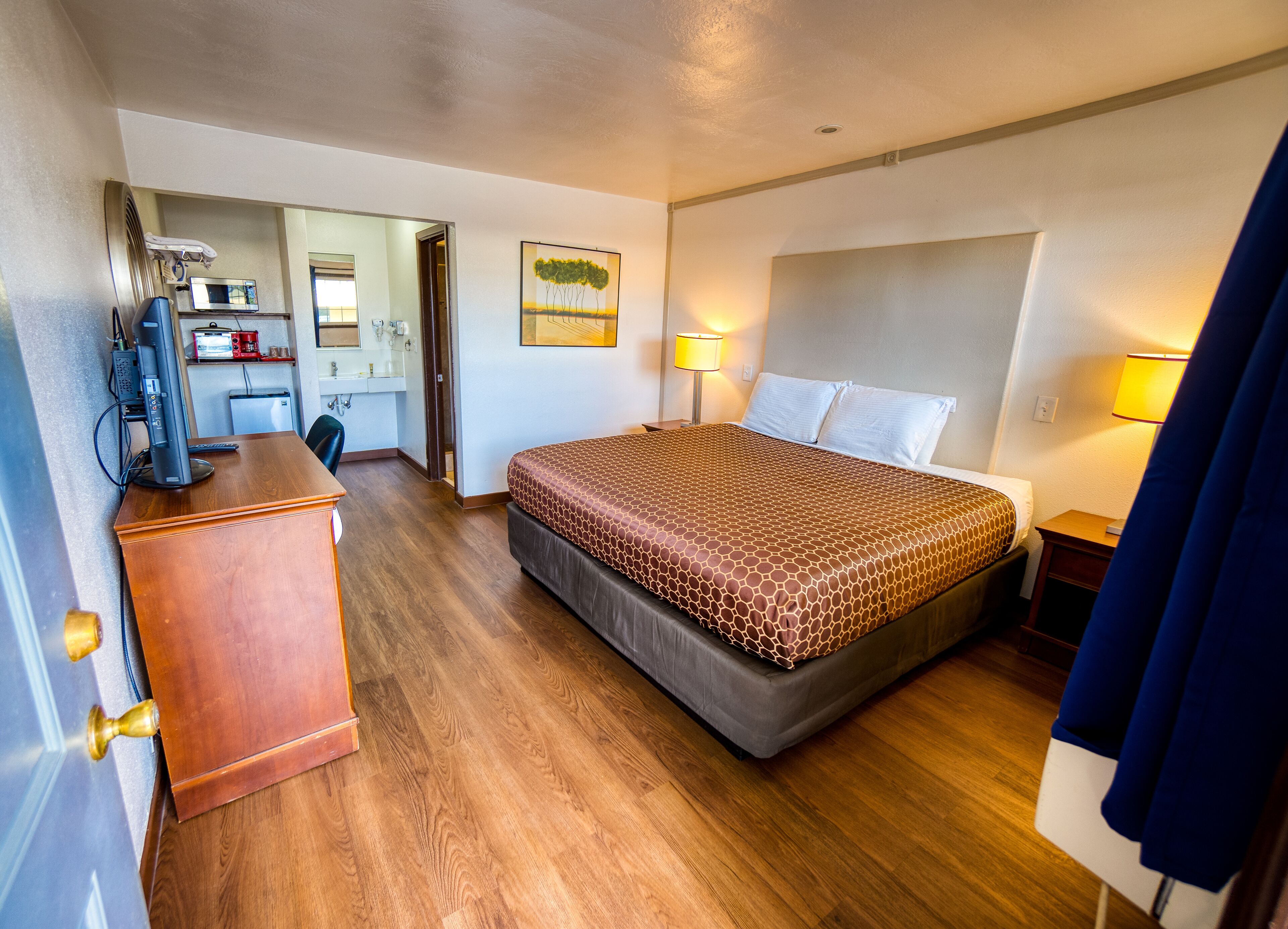 Quarto de hotel com cama, escrivaninha e espaço para cozinha.