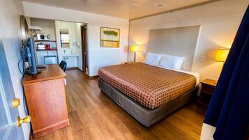 Quarto de hotel com cama, escrivaninha e espaço para cozinha.