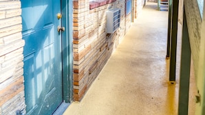 A corridor with a blue door, brick walls, and a wooden ceiling. - Budget Inn Motel (The Dalles)