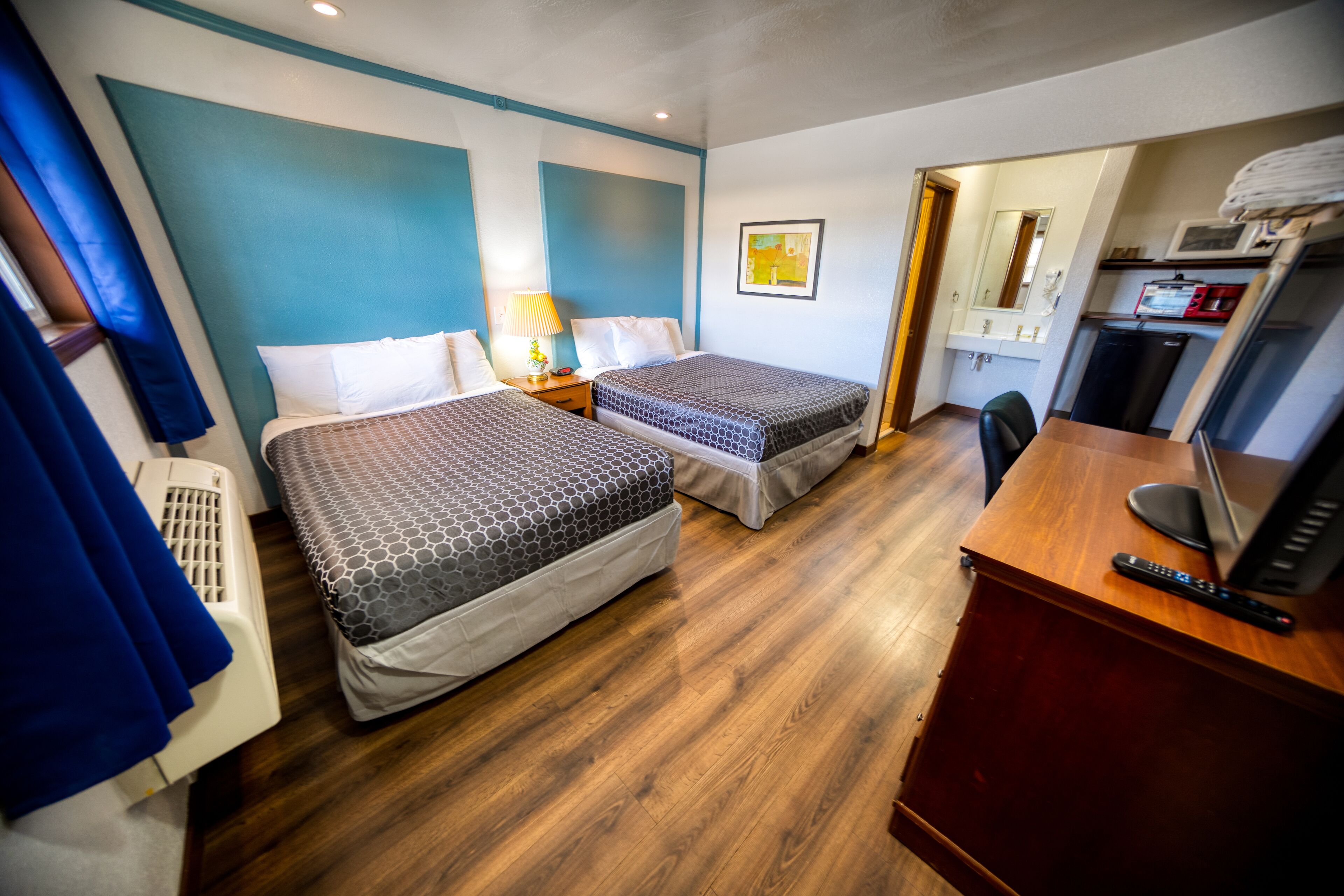 Ett hotellrum med två sängar, ett skrivbord, en stol, en TV och en mikrovågsugn.