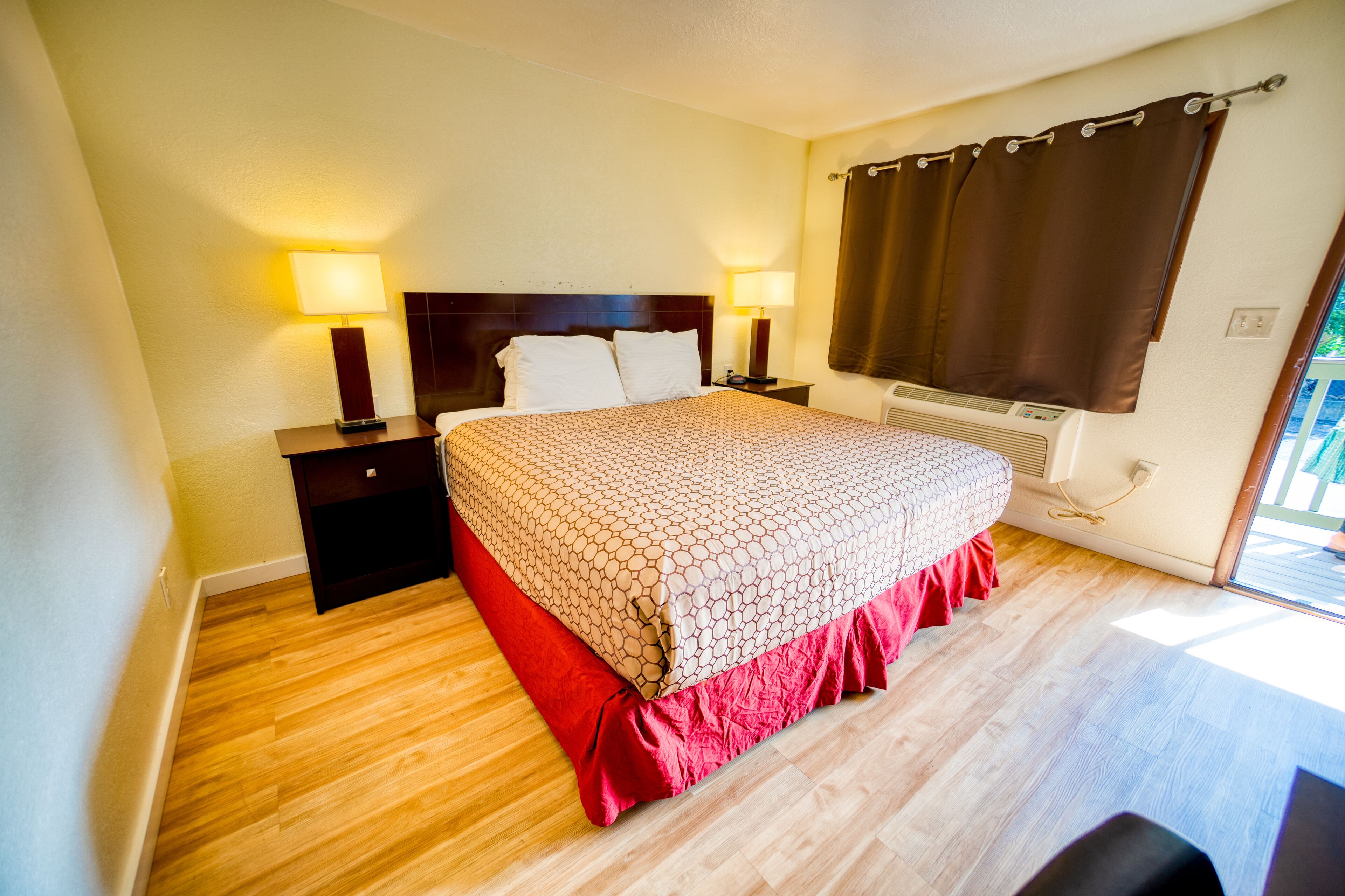 A hotel room with a bed, two bedside tables, a heater, and a window with curtains.