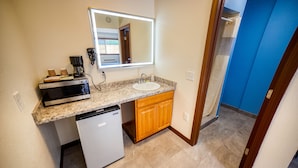 A compact kitchen with a built-in microwave, a small refrigerator, a sink, and wooden cabinets. - Budget Inn Motel (The Dalles)
