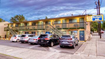A motel with a two-story structure, a parking lot with several cars, and a sign for 'Budget Inn' with amenities like HBO phone and kitchenettes.