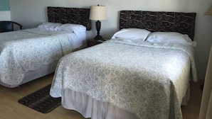 Duas camas de casal com cabeceiras estampadas, uma mesa de cabeceira com abajur e quadros nas paredes.