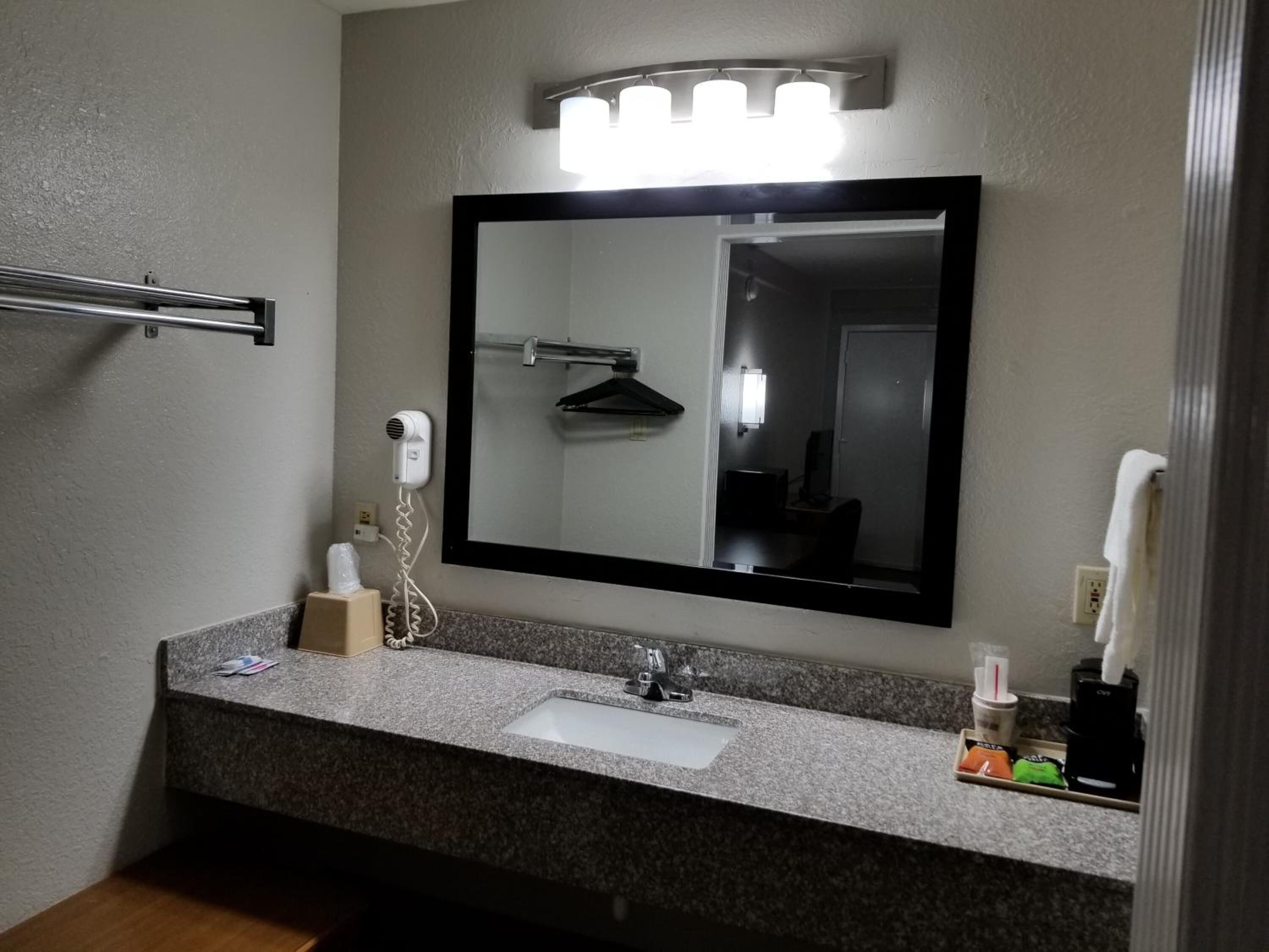 Un bagno con un piano in granito, un lavandino bianco, un portascopevoli, un asciugacapelli e uno specchio illuminato.