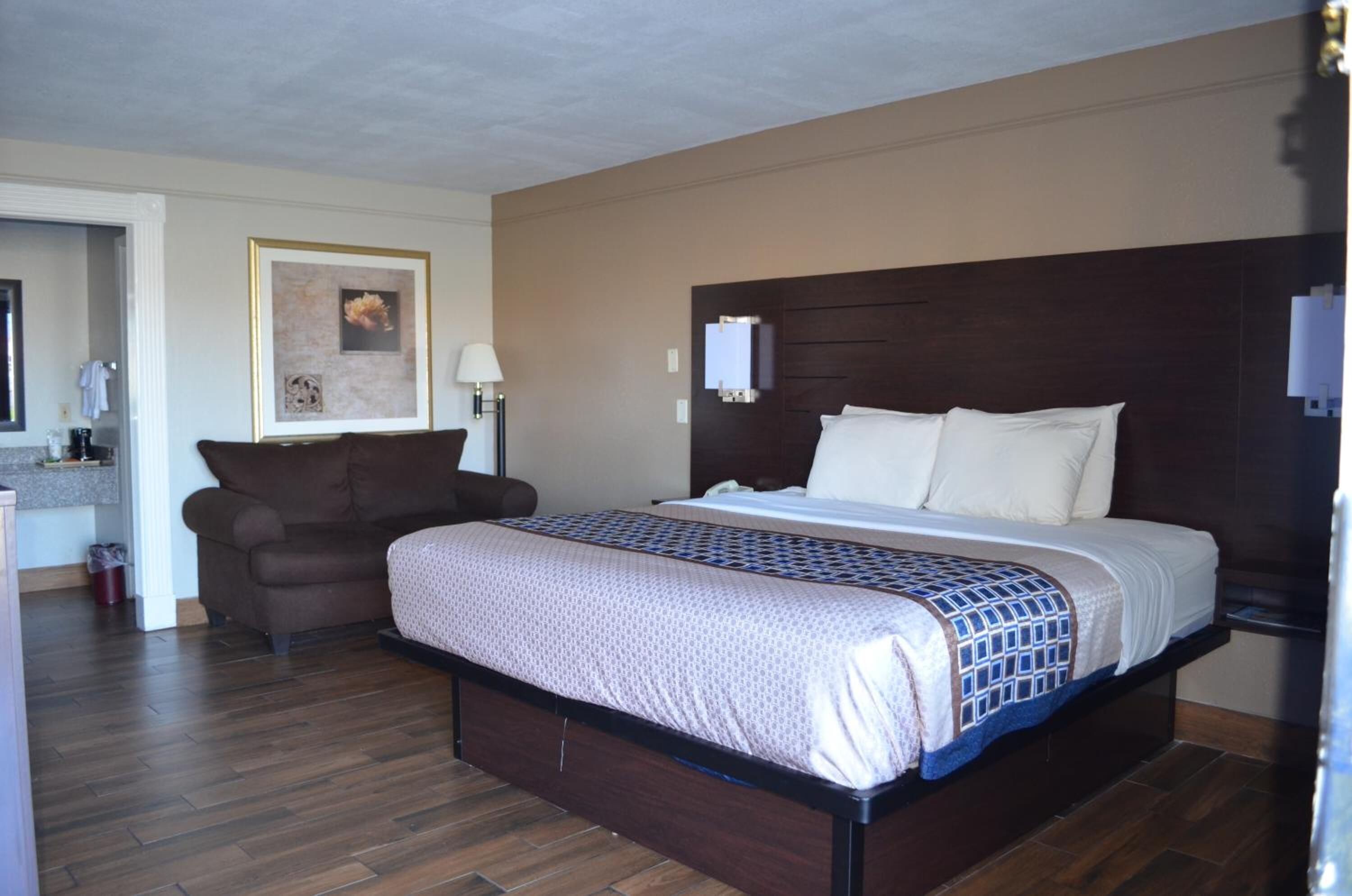 A hotel room with a large bed, a sofa, a small table, and a framed picture on the wall.