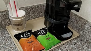 Une machine à café, une tasse et deux dosettes de café sur un plateau.