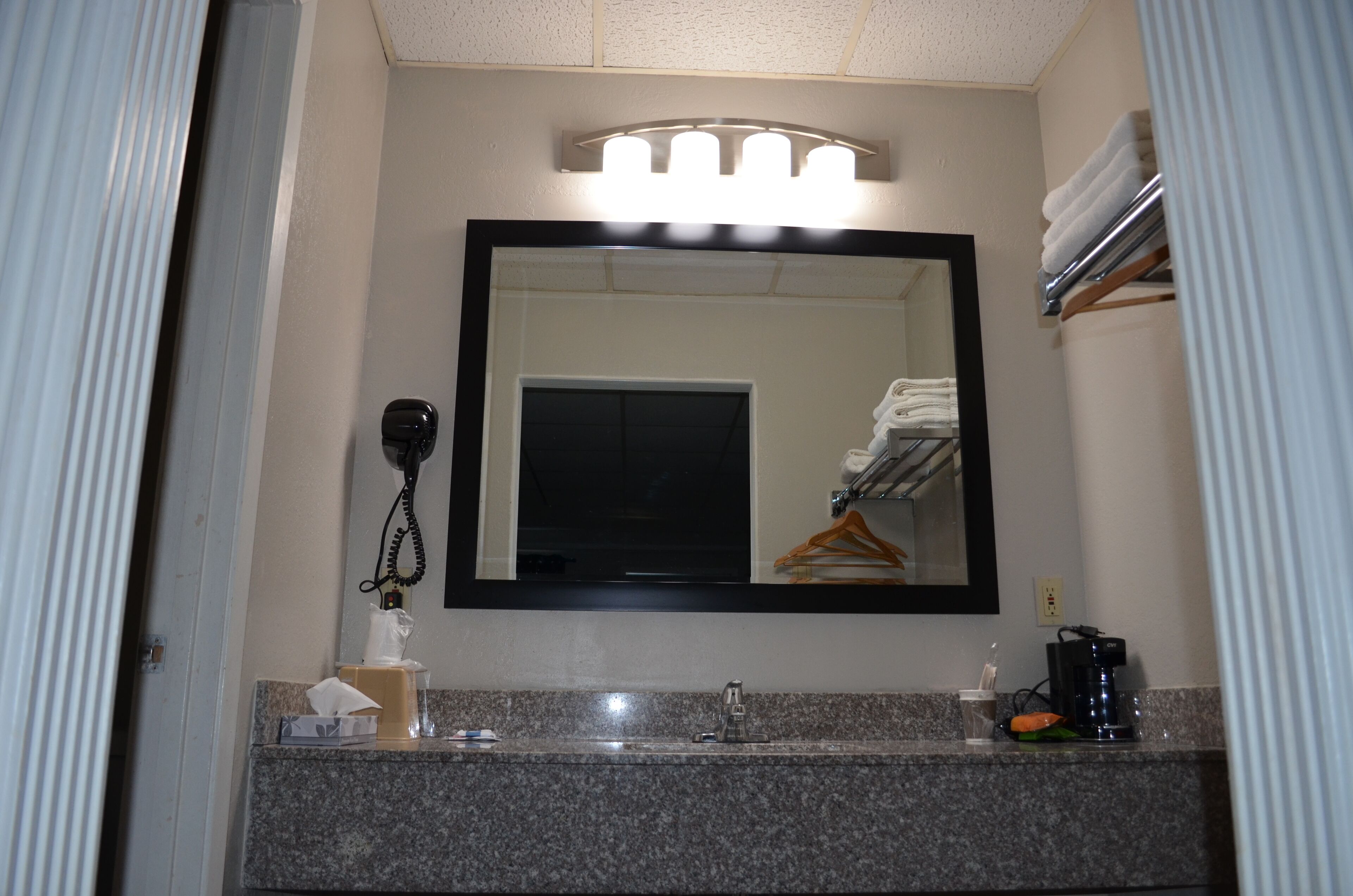 A bathroom with a large mirror, a sink, a towel rack, and a coffee maker.