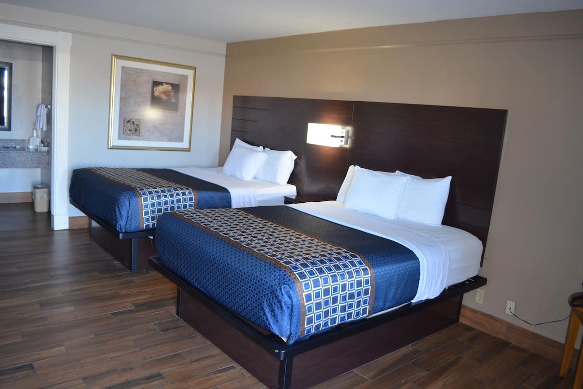 A hotel room with two beds, a wooden floor, a bathroom with a mirror, and a framed picture on the wall.