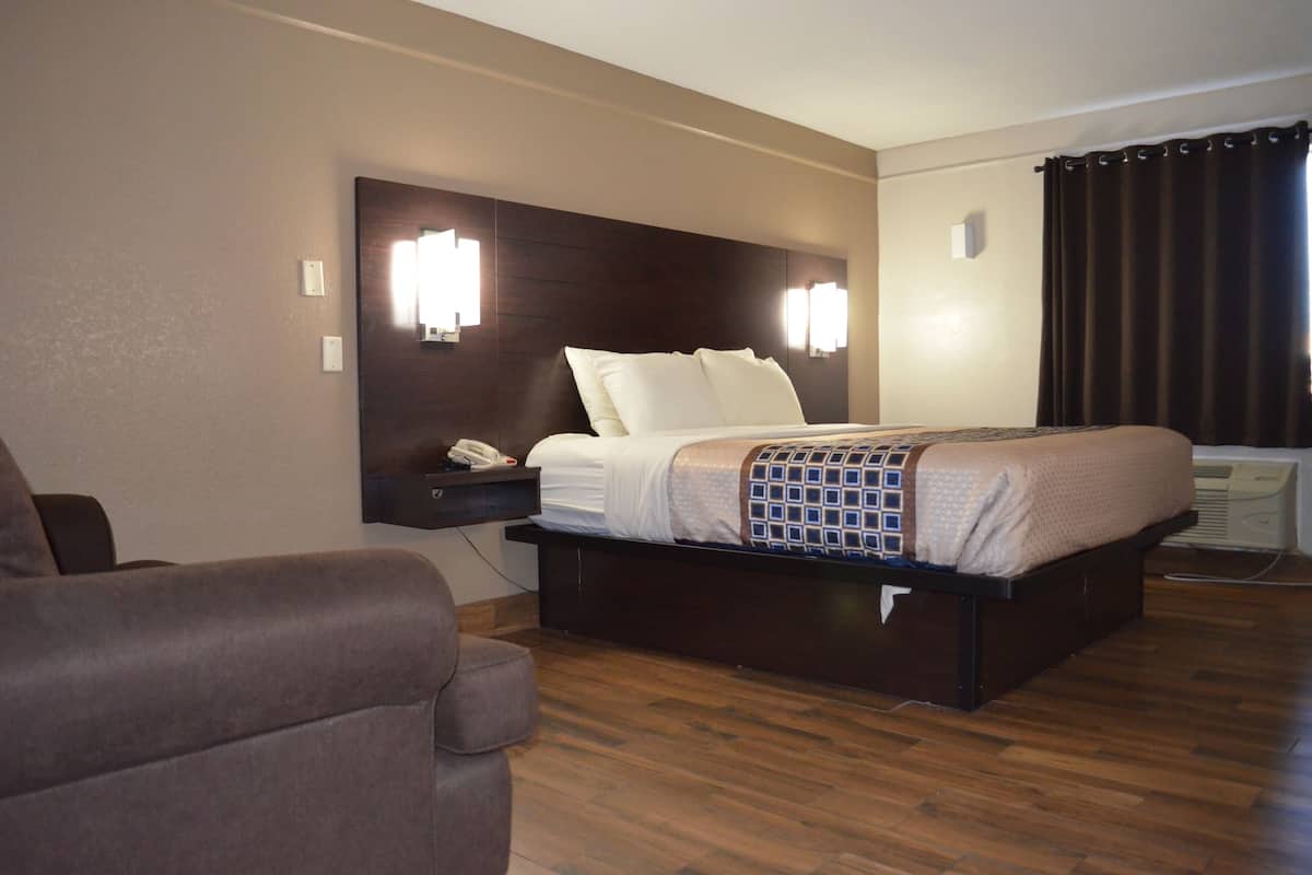 A hotel room with a large bed, a bedside table with a phone, and a chair.