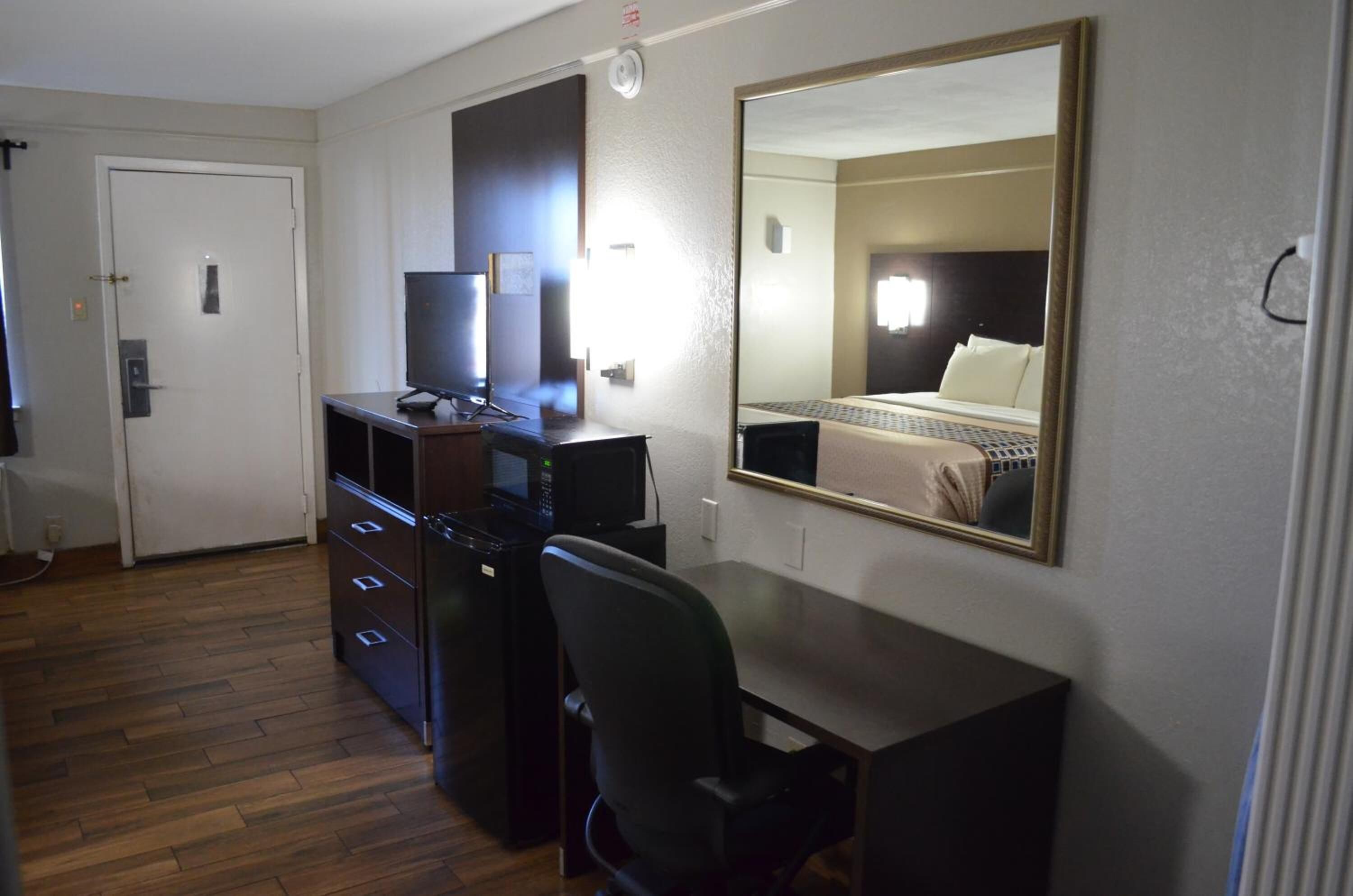 A hotel room with a desk, chair, television, and a large mirror.