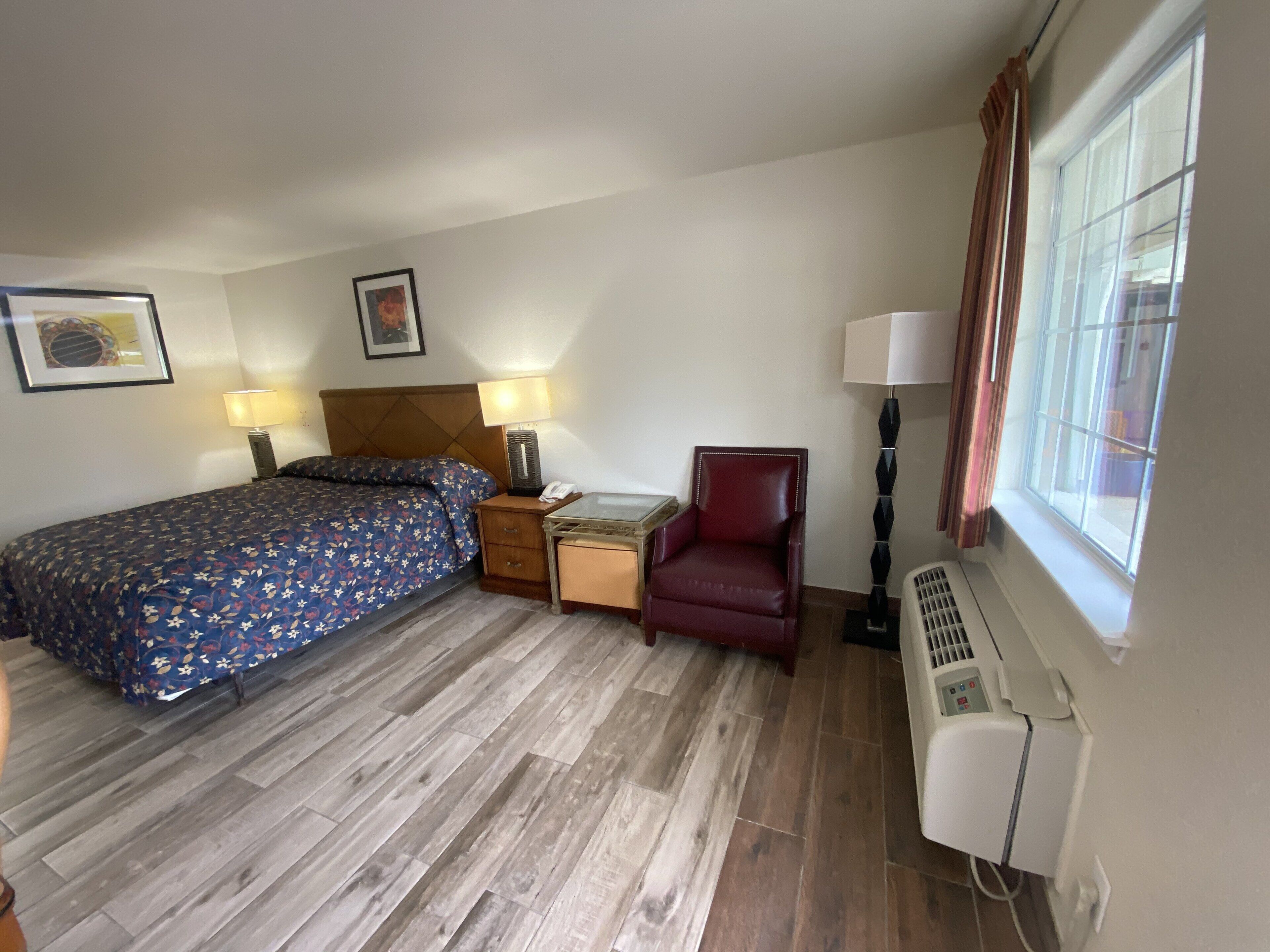 Habitación de hotel con cama, una silla, mesita de noche, lámpara y ventana.