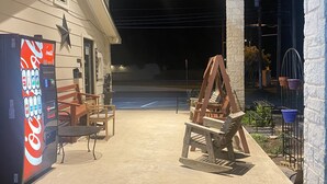 Un espacio de estar al aire libre con una máquina expendedora de Coca-Cola, sillas de madera y un conjunto de columpios.