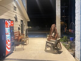 Un espacio de estar al aire libre con una máquina expendedora de Coca-Cola, sillas de madera y un conjunto de columpios.
