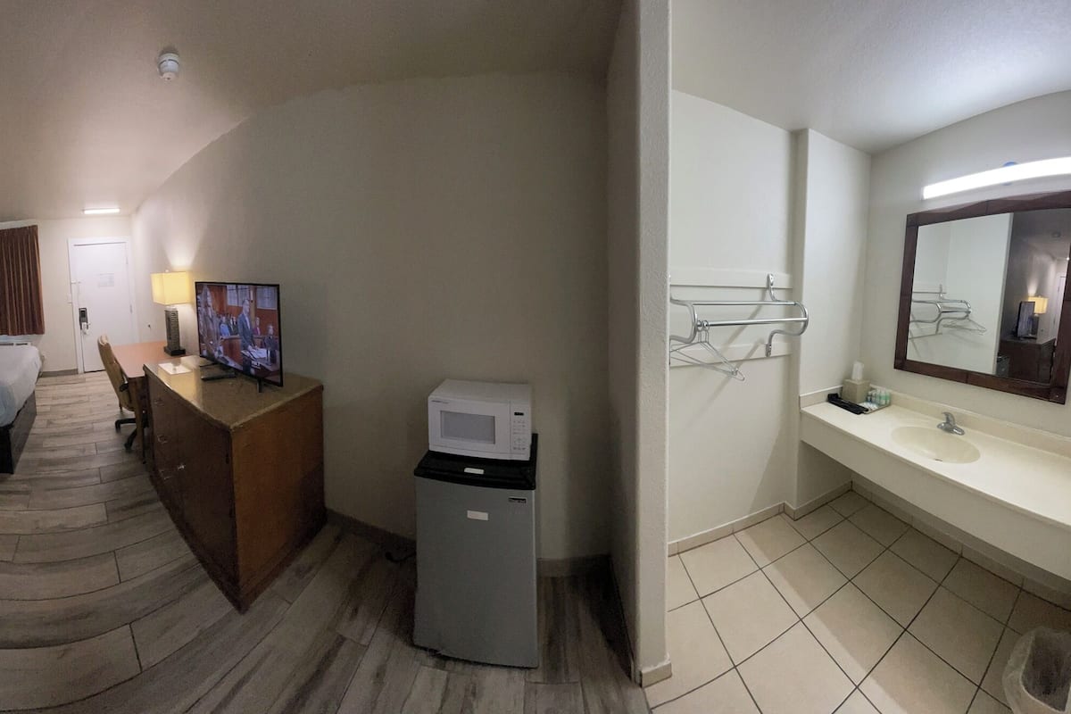 Une chambre d’hôtel avec deux lits, un bureau avec une télévision, un four à micro-ondes et une salle de bain avec un lavabo et un miroir.