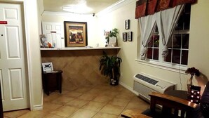 Una habitación con piso de baldosas, una puerta con un letrero que dice 'Solo personal', un cuadro en una repisa, una planta en maceta y una ventana con cortinas.