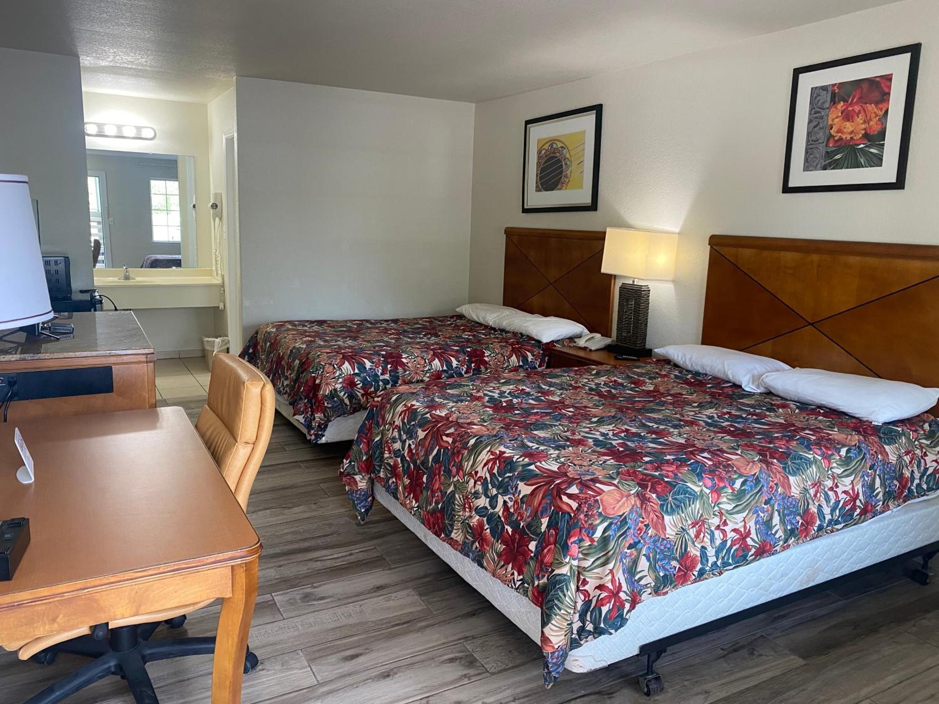 A hotel room with two beds, a desk, and a chair. There are two framed pictures on the wall.