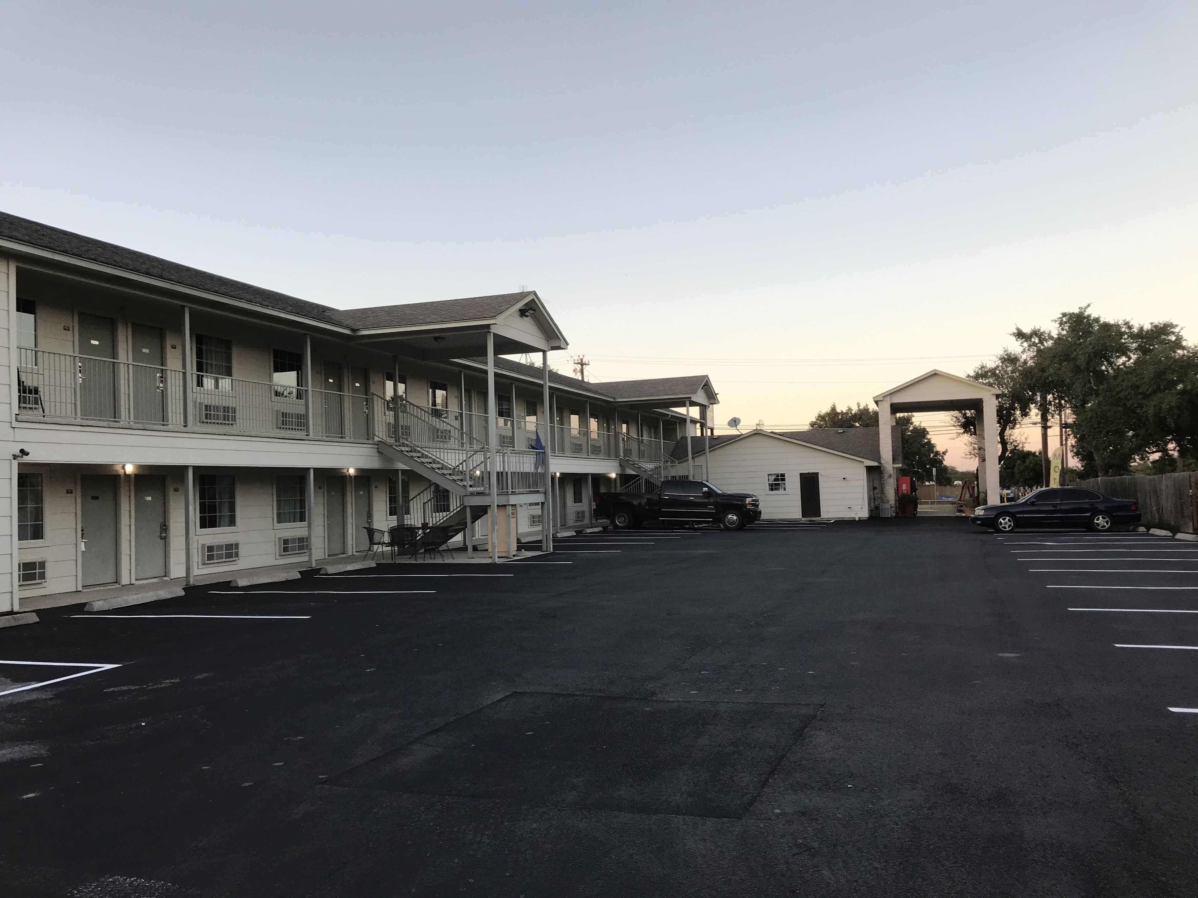 Um motel com vários andares, área de estacionamento coberta e um pequeno edifício com uma placa.