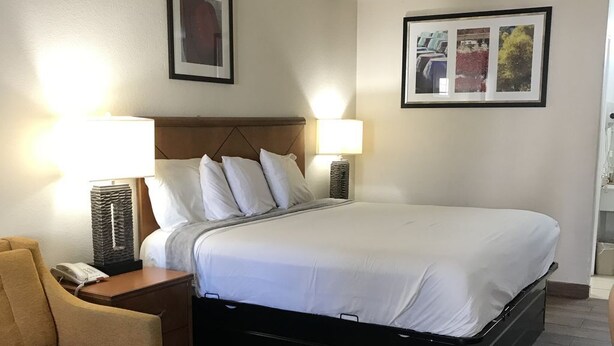 Habitación de hotel ordenada con cama, dos lámparas de noche, una silla y una mesita con teléfono.