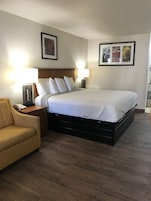 Habitación de hotel ordenada con cama, dos lámparas de noche, una silla y una mesita con teléfono.
