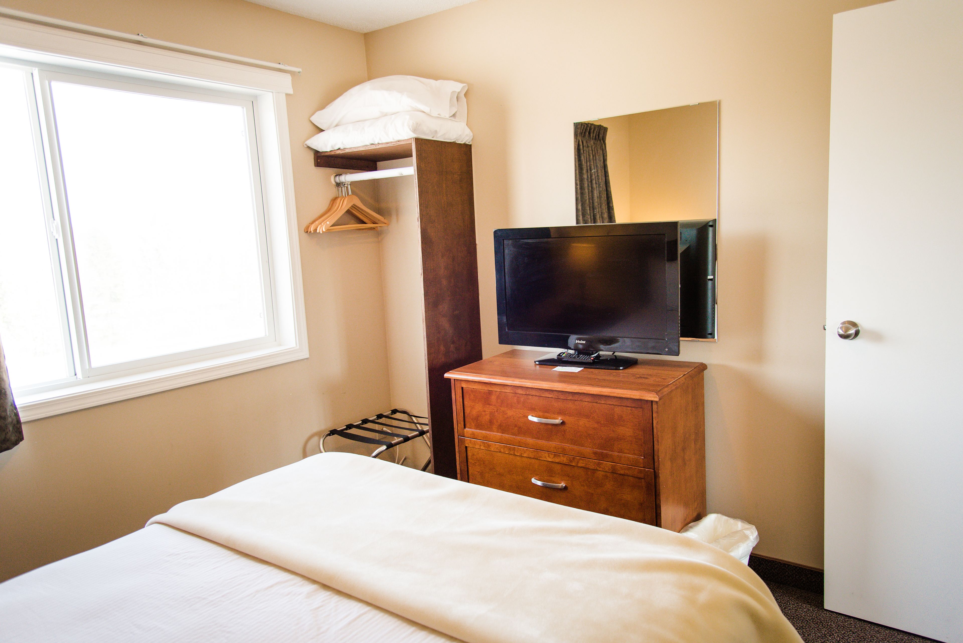 Een hotelkamer met een bed, een houten dressoir, een televisie, een raam en een kledingrek.