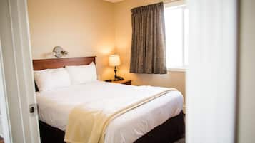 Une chambre d’hôtel avec un lit, une table de chevet avec une lampe et une fenêtre avec des rideaux.