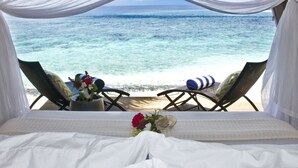 Un letto con vista sull'oceano, due sedie e un'assortimento di fiori.