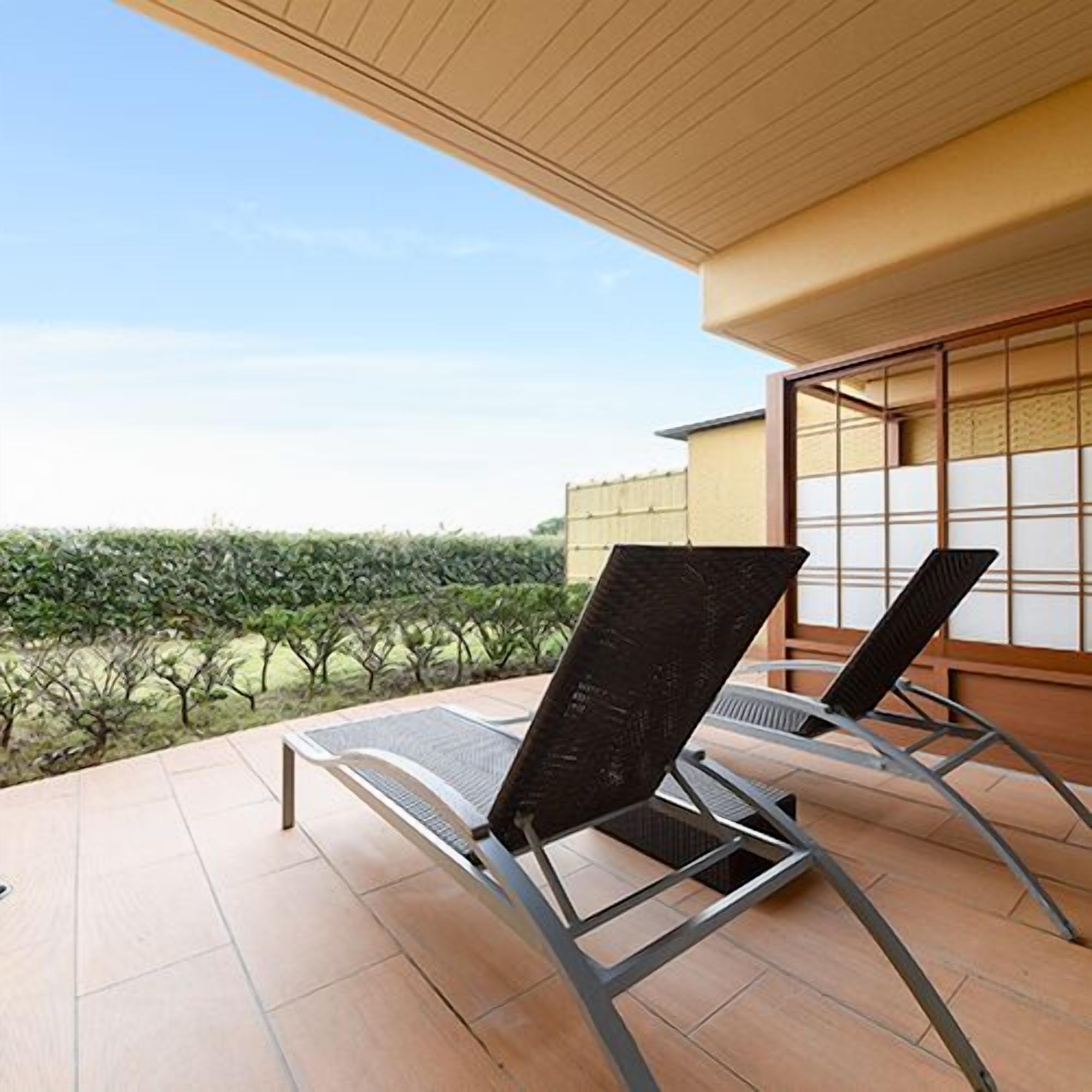 Une terrasse avec deux fauteuils de jardin, un sol carrelé et une vue sur un jardin.