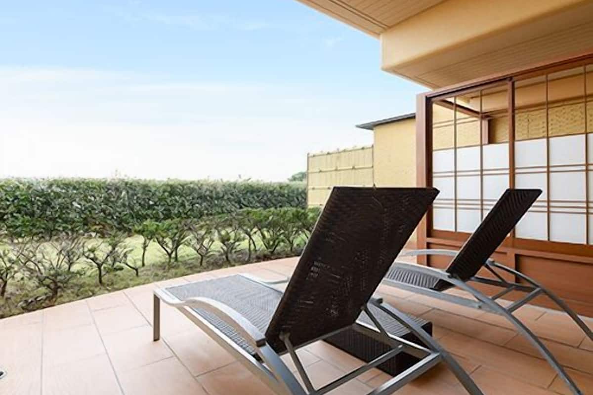 A terrace with two lounge chairs, a tiled floor, and a view of a garden.