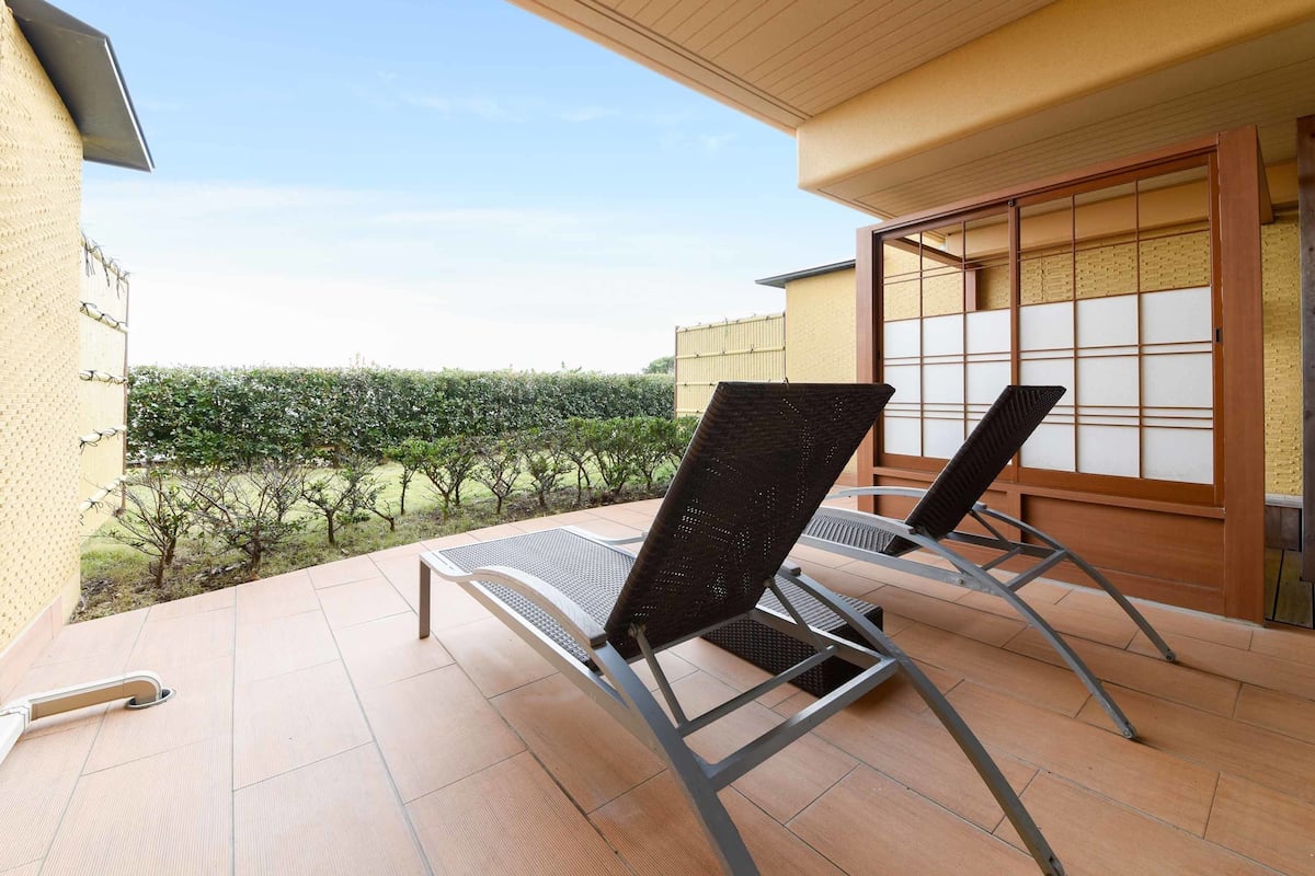 A patio with two lounge chairs, a tiled floor, and a view of a vineyard.