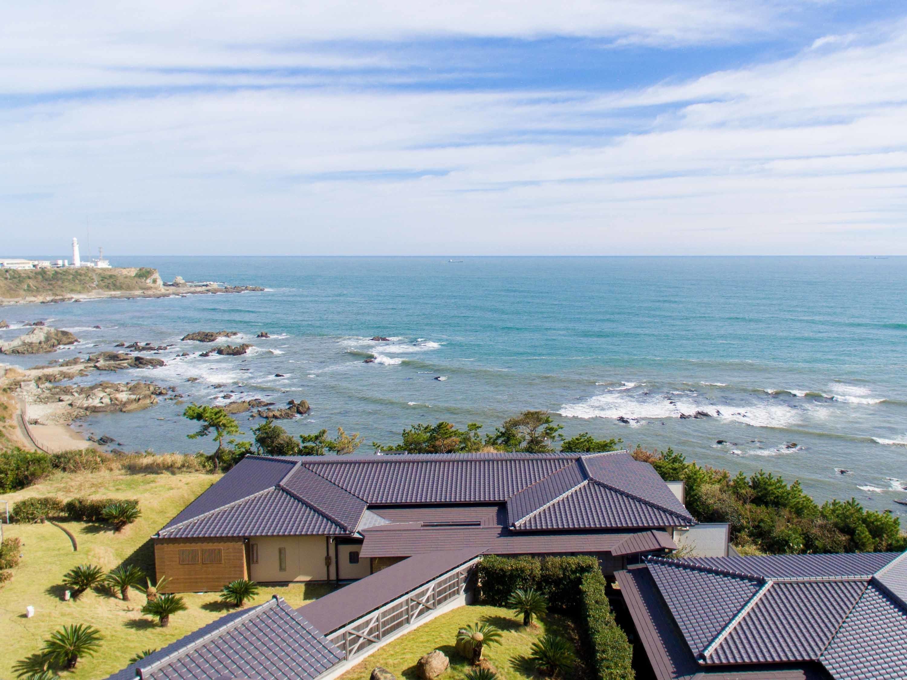 A coastal property with multiple buildings, a rocky shoreline, and a lighthouse in the distance.