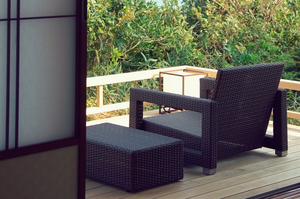 Une terrasse dotée de meubles en osier, notamment une chaise et un pouf, ainsi qu’une petite table.