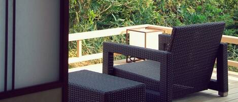 Une terrasse dotée de meubles en osier, notamment une chaise et un pouf, ainsi qu’une petite table.
