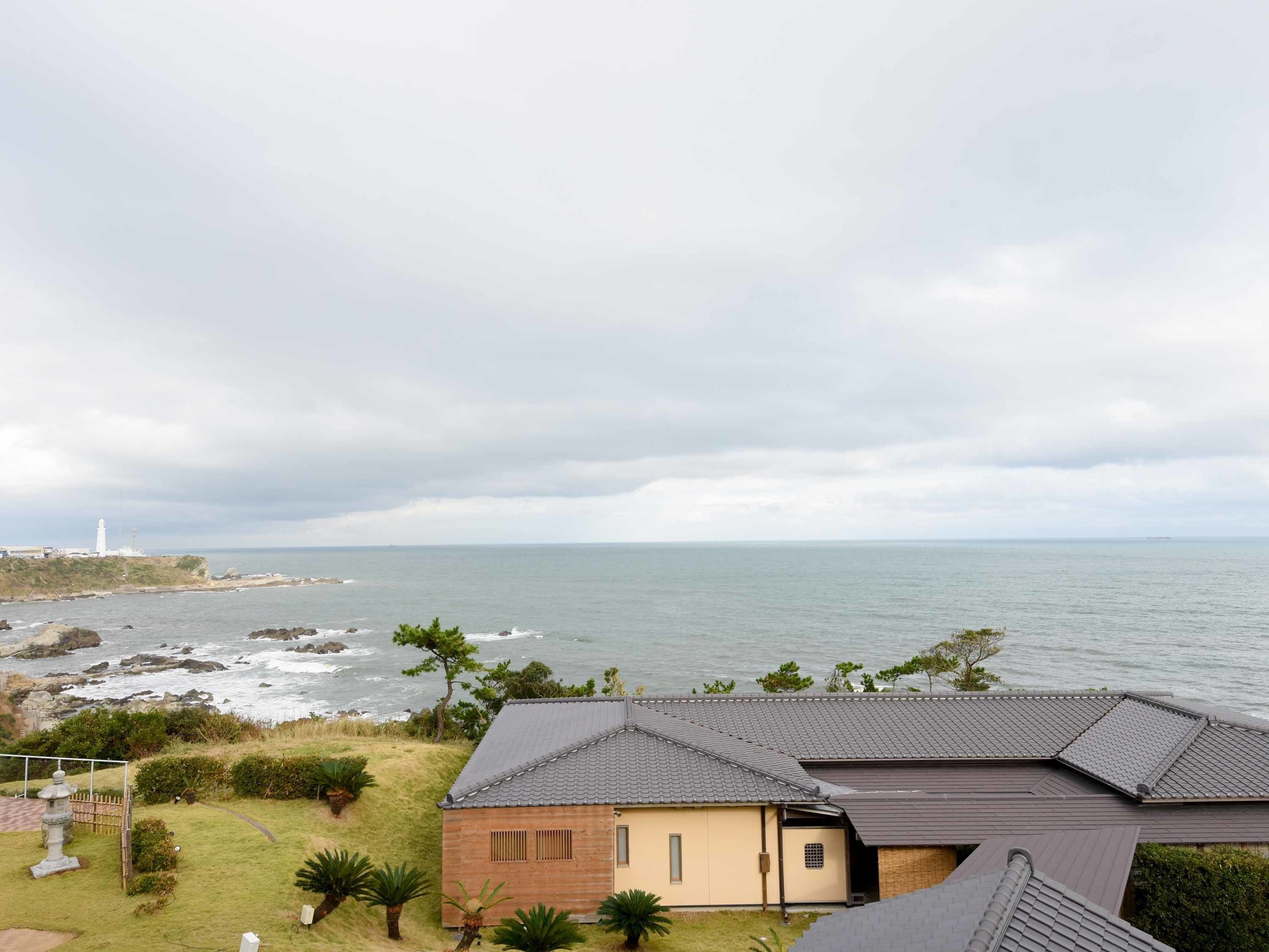 A coastal house with a view of the sea and a lighthouse in the distance.