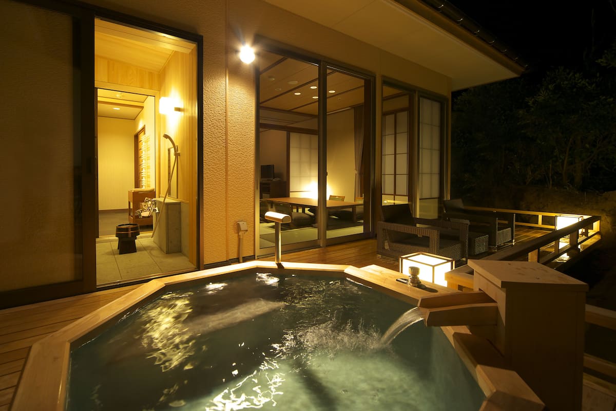 A hot tub area with a wooden deck, a glass door leading to a room, and a small table with a lamp.