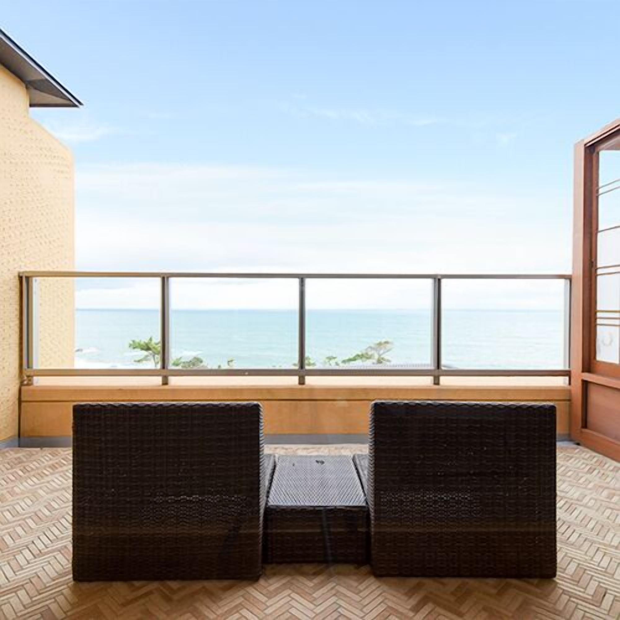 Ein Balkon mit zwei Korbstühlen, Holzboden und Blick auf das Meer.