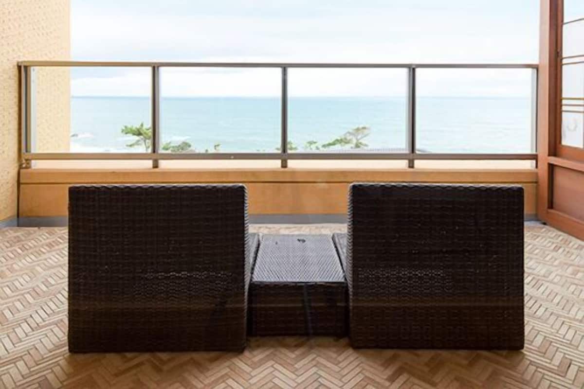 A balcony with two wicker chairs, a wooden floor, and a view of the sea.