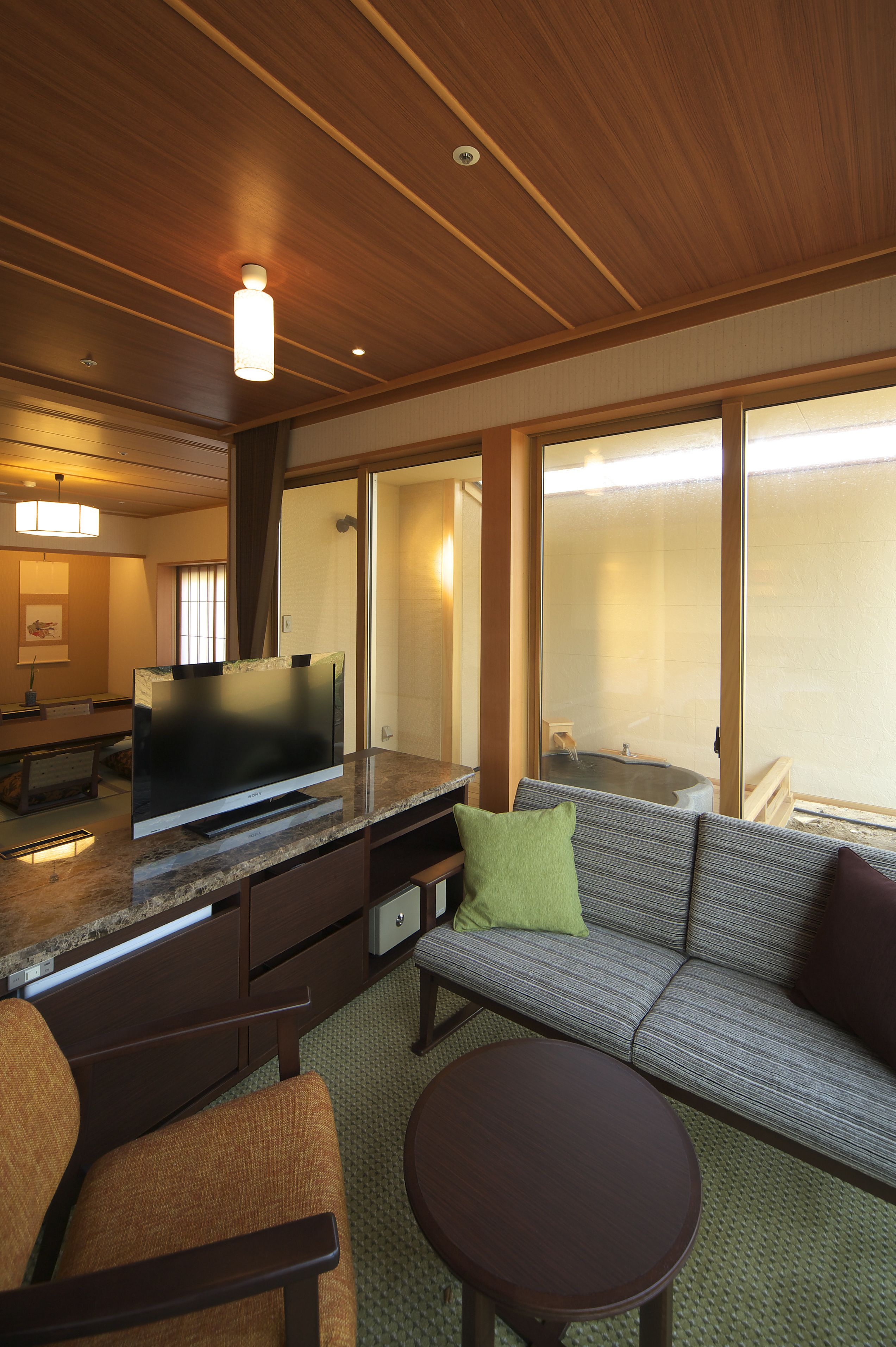 A modern hotel room with a flat-screen TV, a sofa, a small table, and a large window with a view of the outside.