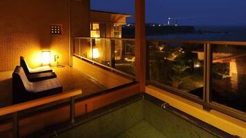 A balcony with a seating area and a view of the sea at dusk.