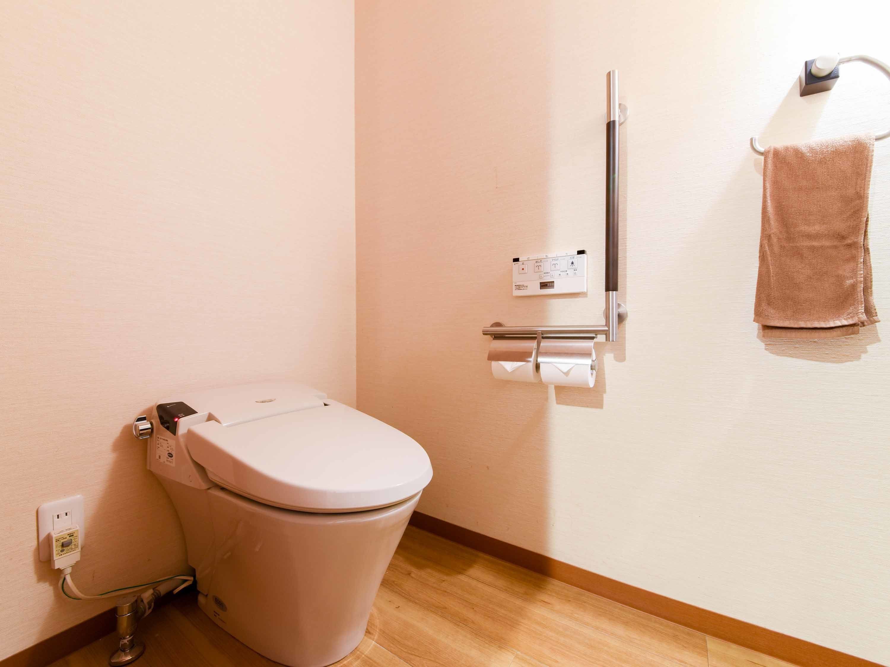 A modern bathroom with a toilet, a hand dryer, and a towel hanging on a rack.