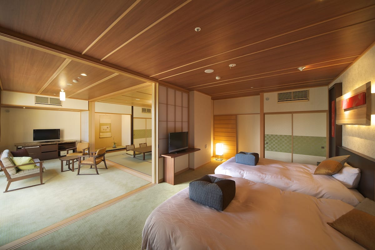 A hotel room with two beds, a desk with a television, and a seating area with chairs.