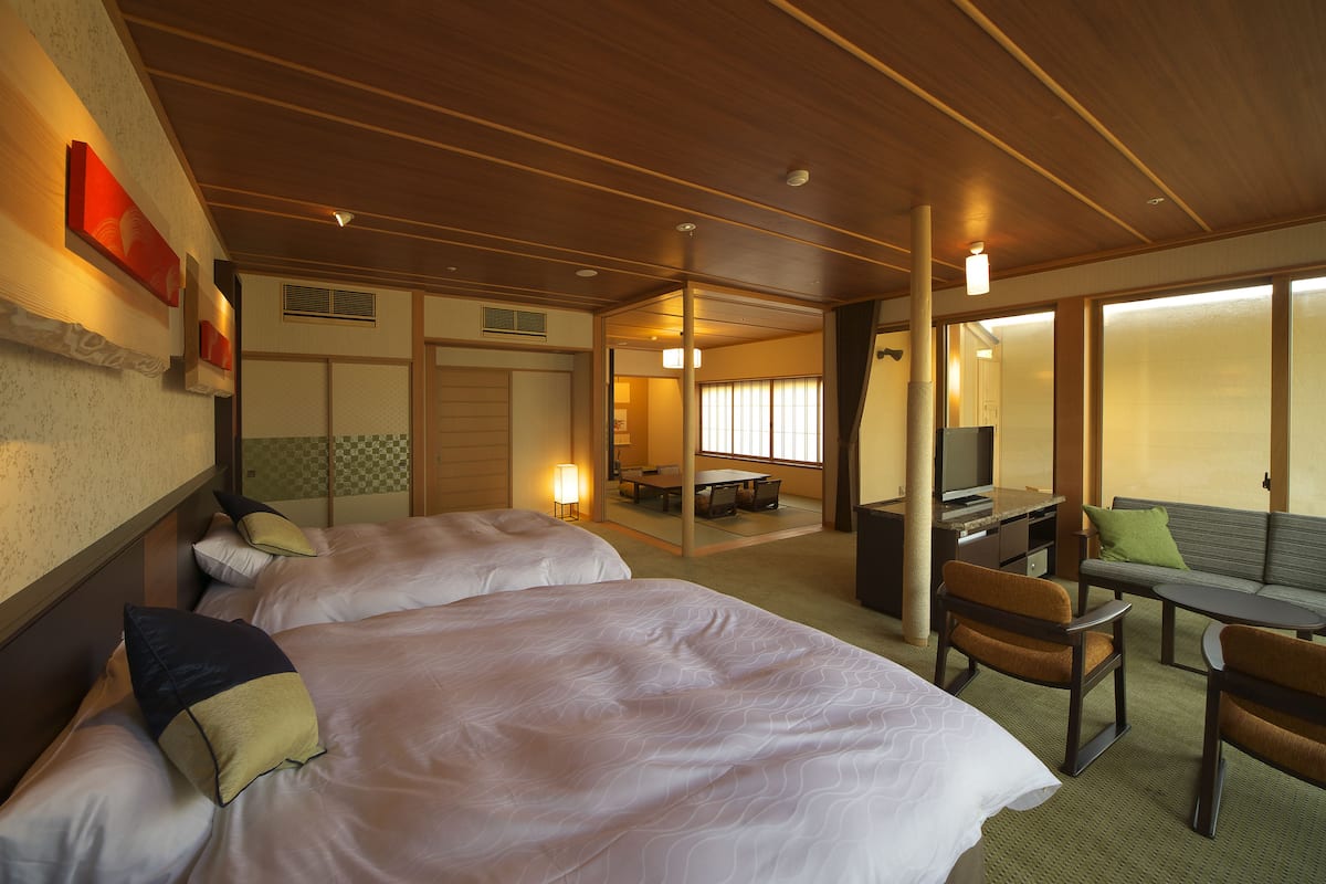 A hotel room with two beds, a desk, a chair, and a sofa.