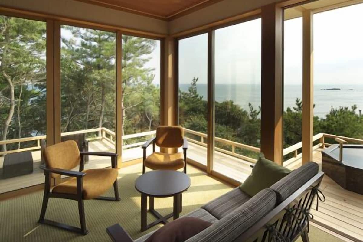 A spacious room with a large window offering a view of the sea, a wooden ceiling, and a seating area with a sofa and chairs.