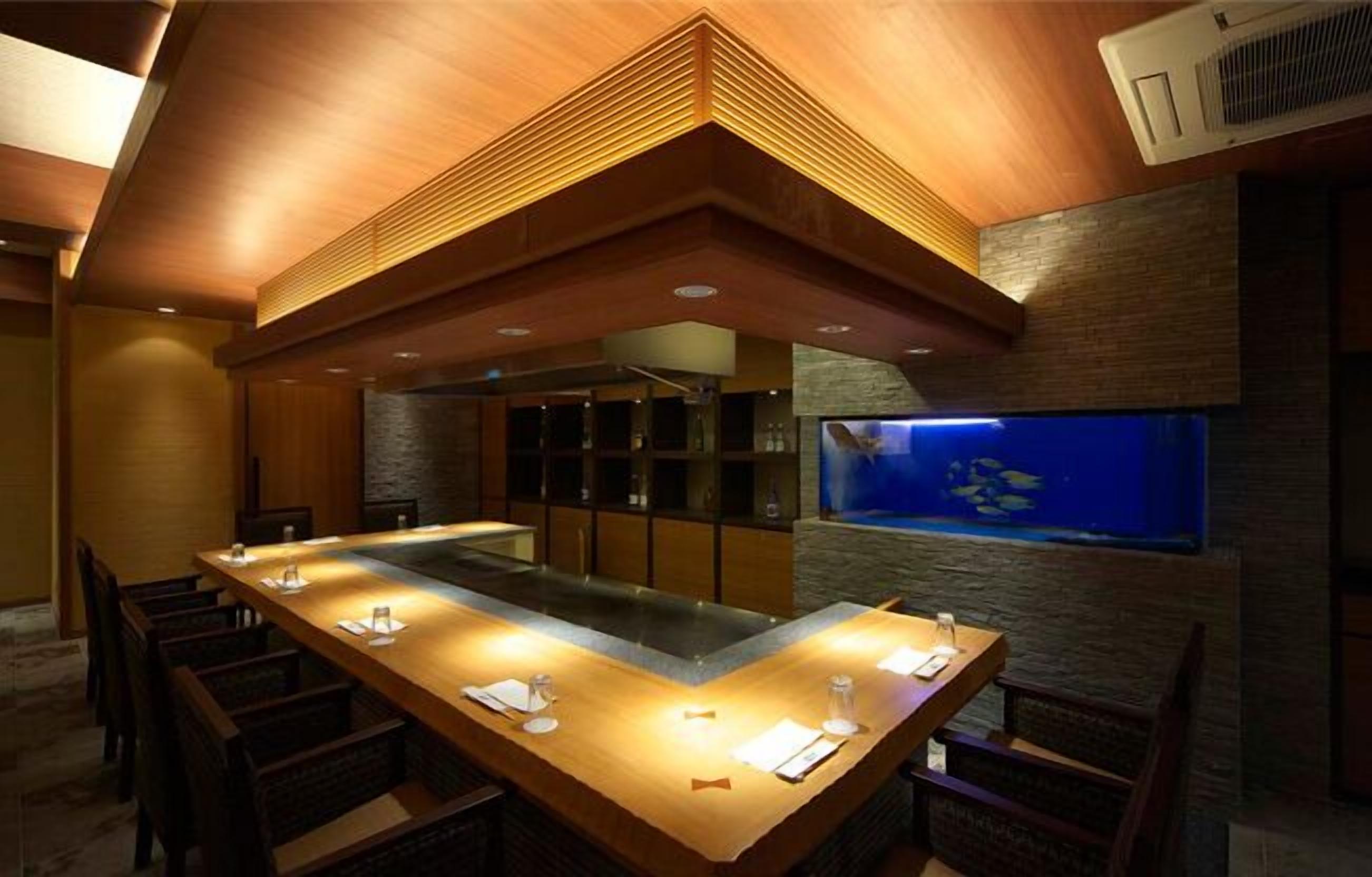 A restaurant with a long wooden table, chairs, and a fish tank on the wall.