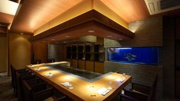 A restaurant with a long wooden table, chairs, and a fish tank on the wall.