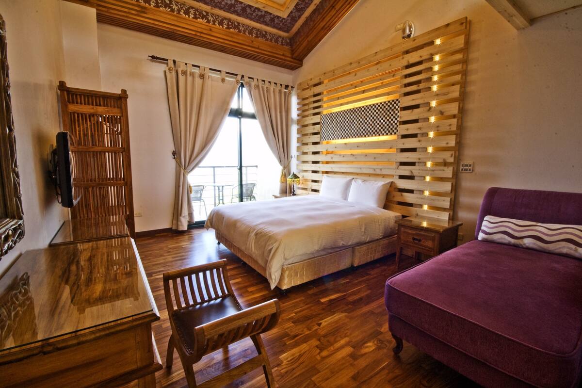 A bedroom with a wooden bed, a wooden dresser, a wooden chair, and a purple sofa.