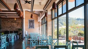 Un restaurante con una mesa larga y sillas, un muro de piedra y vistas a un paisaje verde.