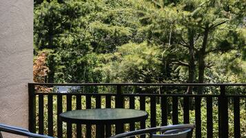 An outdoor patio with a round table and two chairs, surrounded by a wooden railing, overlooking a forested area.