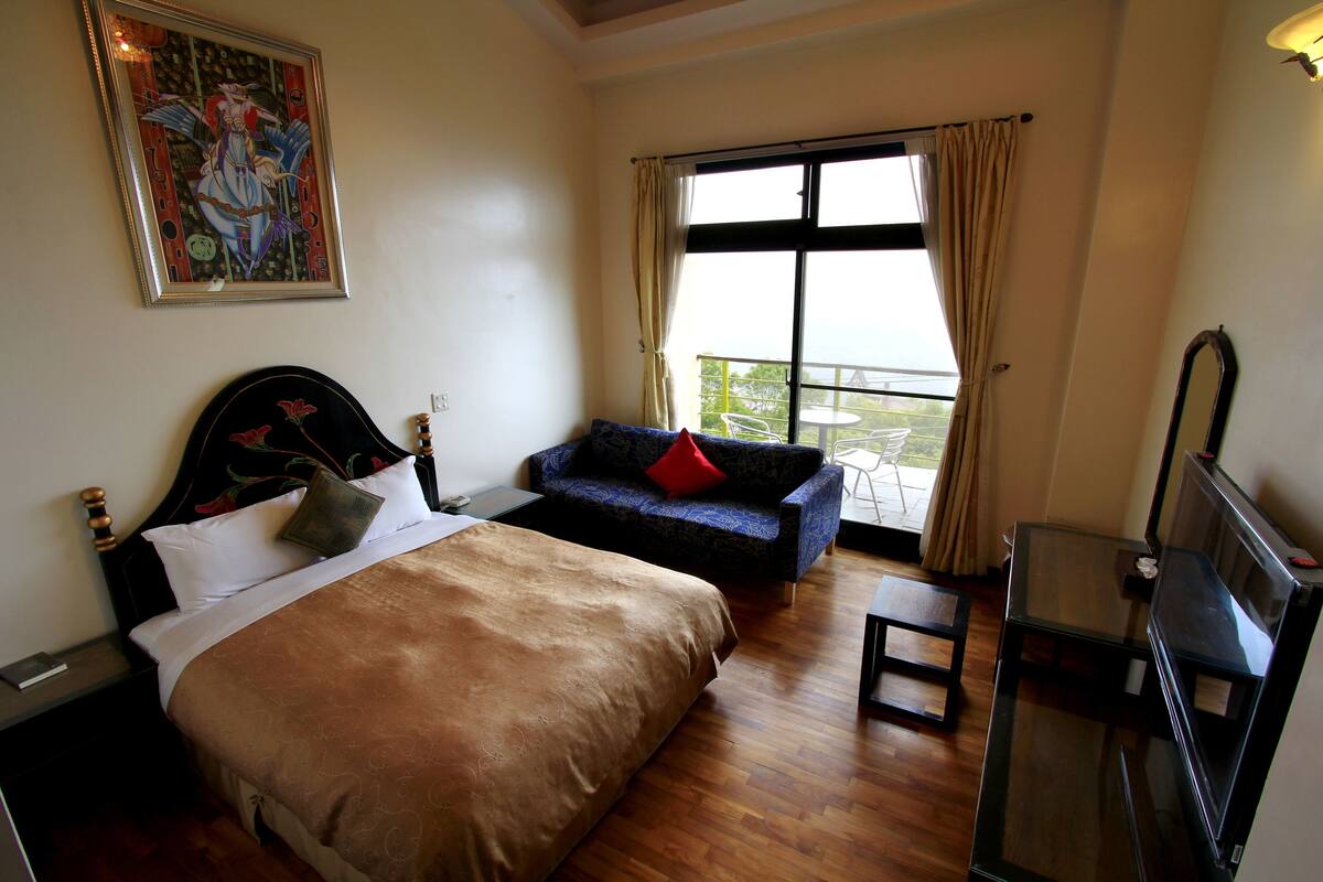 A hotel room with a large bed, a sofa, a balcony with a table, and a TV.